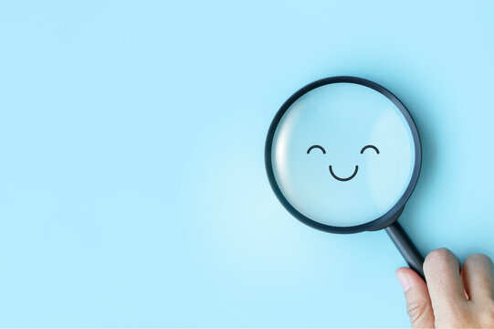 Hand holds a magnifying glass over a smile face, happy satisfaction survey, positive, good, wellness and relax. symbolizing the search for positivity among neutral. world mental health day concept.