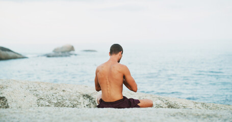 Man, yoga and back by beach with meditation, peace and mindfulness on rock in morning for wellness. Person, breathing space and self care routine with zen, chakra and water by ocean in New Zealand