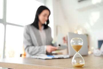 Hourglass on desk against businesswoman working with laptop in office, closeup
