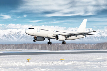 White passenger plane landing at winter airport on the background of mountains