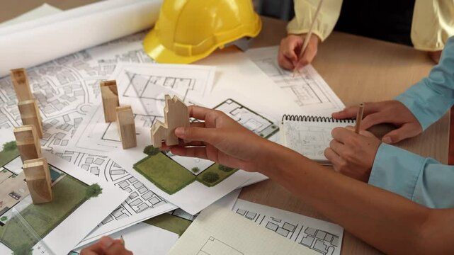 Architect and engineer consider or discuss about building construction using blueprint on table with architectural document, measurement tool and wooden block scatter around at office. Delineation.
