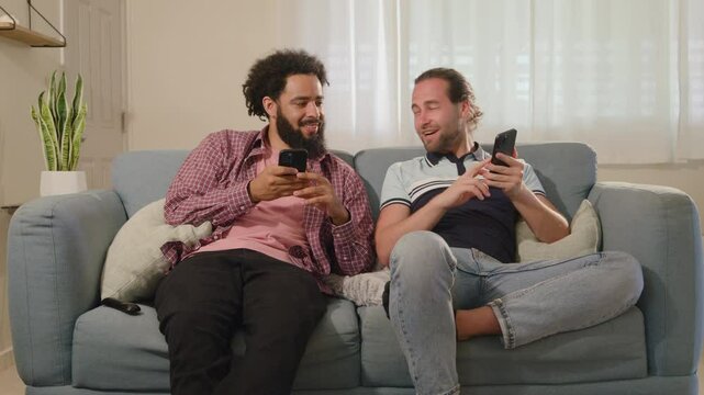 Two friends are sharing a lighthearted and cheerful moment while using their smartphones on a cozy couch, thus enhancing their connection and interaction through technology in their everyday lives
