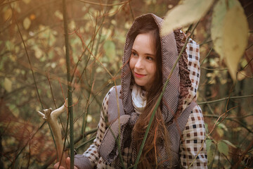 A woman with long hair wearing a hood with a wooden staff in the woods