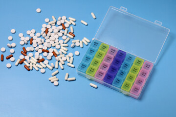 Colorful weekly pill organizer and assorted pills lying on a blue background