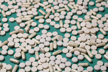 White pills and capsules lying on turquoise background representing healthcare and medicine