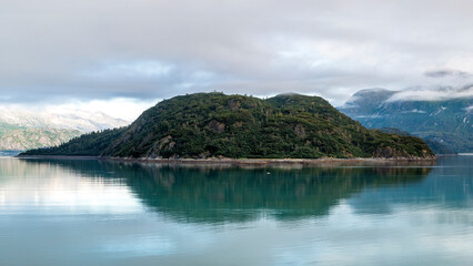 An elegant island covered in rich greenery stands proudly in calm waters, perfectly mirrored, illustrating the beauty of nature's reflections and the allure of untouched landscapes.