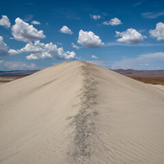 A mesmerizing sandy dune with distinct tracks left by footprints, contrasting beautifully with a vibrant blue sky adorned with fluffy clouds.