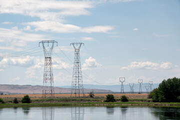 A scenic view showcasing tall power lines stretching across a tranquil landscape, with a river in...