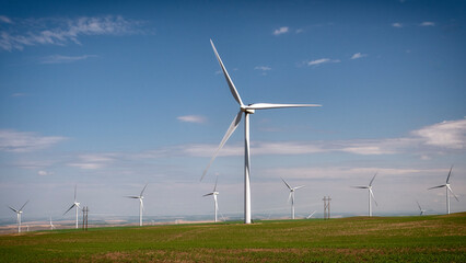 This striking image features wind turbines scattered across a vibrant green landscape under a clear...