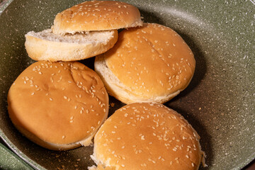Toasted sesame seed buns arranged in a frying pan, showcasing the preparation of fresh bread for burgers or sandwiches in a homey style.