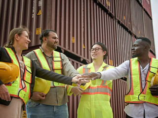A diverse team of logistics professionals in safety vests shaking hands and communicating, working together in a warehouse with cargo containers in the background.