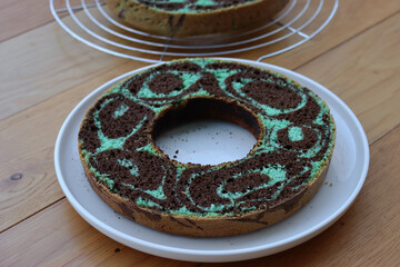 Cut in half mint and chocolate marble cake on a white plate on wooden table ready to be filled with chocolate cream