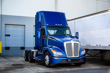 Blue bonnet day cab big rig semi truck tractor with roof spoiler standing beside loading in...