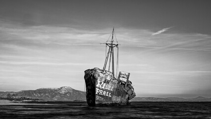 An intriguing shipwreck stands alone on a deserted beach, with its rusting hull and eerie...