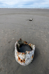 A weathered, rusty pipe sits prominently on the sandy beach, symbolizing the intersection of nature and man-made structures, and raising questions about environmental impact.