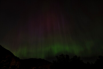 The mesmerizing Northern Lights illuminate the twilight with vibrant hues of green and purple, creating an enchanting spectacle against the dark silhouette of the mountains.