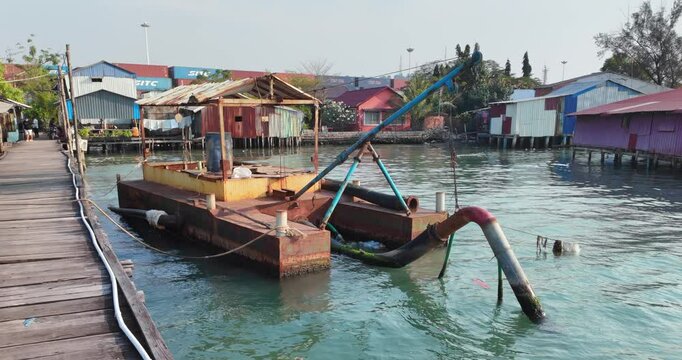 close up of a dredging vessel rests by a wooden pier, equipped with a corrugated metal shelter and large pipes for dredging work.