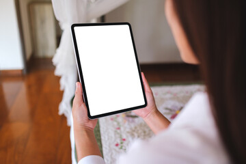 Mockup image of a woman holding tablet with blank desktop white screen on the bed at home
