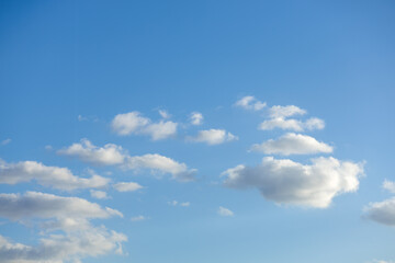 Soft blue of the morning sky backs dreamy white and delicate gray hued cotton ball clouds forming an arch pattern in the sky.