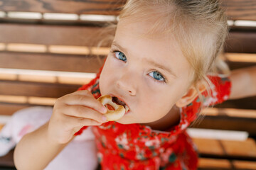 Little girl eating a crispy bagel while sitting on a wooden bench
