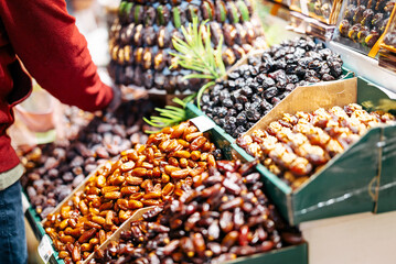 A vendor arranges a variety of stuffed dates at a market stall. A decorative tower of dried fruits, including nuts and colorful fillings, creates an inviting and vibrant display.
