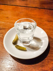 A shot glass of alcohol and pickles on a plate