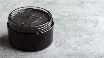 A sleek, black jar containing a dark substance, positioned on a textured gray surface, suggesting a beauty or skincare product.