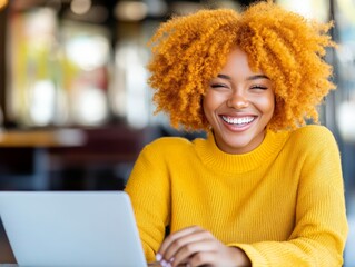 Confident young woman with bright yellow curly hair sitting at a desk in a modern office working on a laptop in a creative workspace