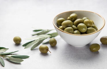 Fresh green olives in a bowl with olive branches on marble table