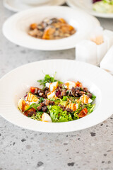A fresh salad in a white bowl, featuring greens, diced vegetables, and drizzled dressing, served on a textured gray surface.