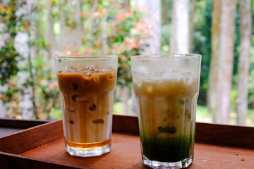 Ice coffee latte and ice matcha latte with trees background. Two cold drinks ordered at an outdoor cafe on the edge of the forest. Chilling and Relaxing at cozy place. Drink and Beverages. Tasty