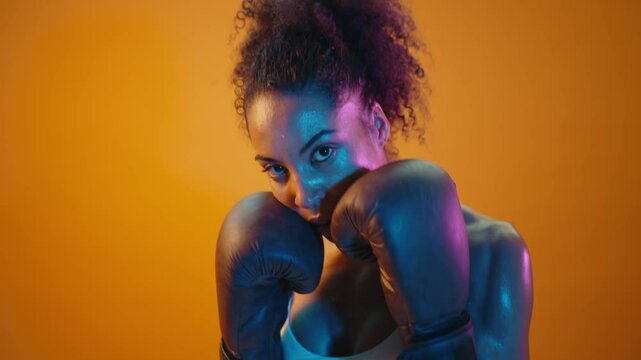 Sportive black hispanic woman wearing sportswear training boxing in fitness studio, colorful dramatic lighting - African-american female athlete doing sport workout	