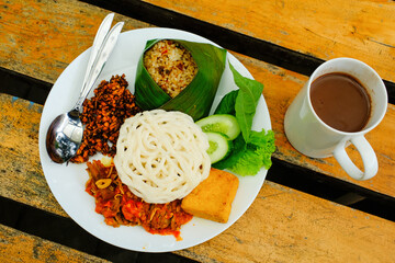 Sundanese cuisine photo with wooden table background. A set of Delicious Dishes consisting of Tutug Oncom rice, Fried Tofu, and Beef Gepuk with red chili sauce, complete with White Cracker. Tasty Food