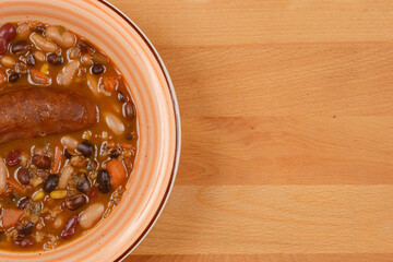 A top-down shot of a bowl of bean stew with sausage, showcasing a hearty meal on a wooden surface