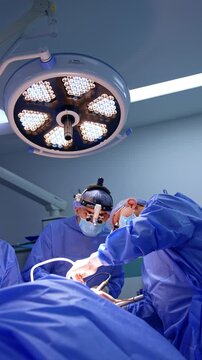 Switched on round lamp on the ceiling of the modern surgical room. Surgeons in surgical loupes perform operation under the bright illumination equipment. Low angle view. Vertical video.
