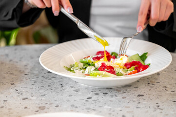 A close-up of a fresh salad being served, featuring vibrant vegetables and a perfectly cooked egg. Hands, holding fork and knife, elegantly prepare to enjoy the meal.