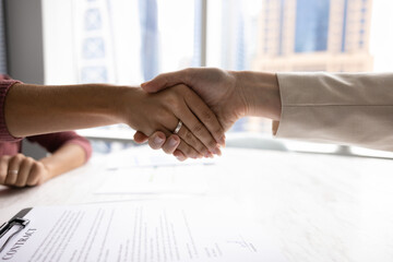 Two female business partners shaking hands over paper contract on meeting table, ending...