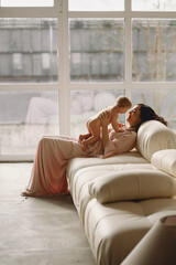 Beautiful happy mother with baby girl in her arms. The concept of a happy family, motherhood. Mother playing with her baby indoor near window.