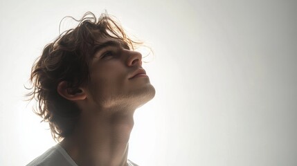 A young man face, bathed in the soft glow of natural light, stands alone against a pristine white backdrop, a solitary figure in a world of his own.