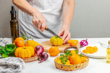 A woman is preparing a tomato salad. Ripe vegetables, herbs, aromatic spices, olive oil