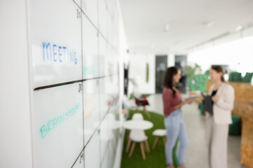 Close up of scrum board in contemporary co-working space with two female business colleagues...