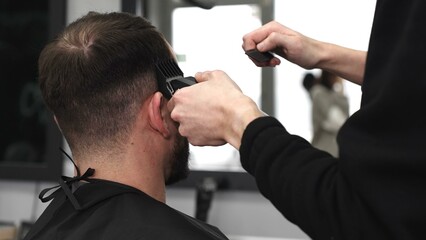Skilled barber trimming client's hair using electric razor, creating contemporary hairstyle in...