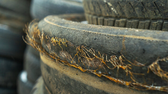 Close-up view of discarded old car tires outdoors, showcasing a pile of used tires ready for recycling. Highlighting environmental concerns and rubber waste management. Defocused background.