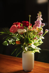 A bouquet of beautiful flowers in a vase, placed on a table at home. The soft morning light gently illuminates the flowers, creating a warm and serene atmosphere in the room.