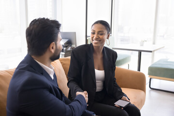 Two business partners, colleagues or teammates dressed in formal suits shake hands. African and...