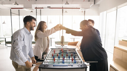 Four colleagues engaging in foosball game in co-working, giving each other fist bump, celebrating win, enjoying friendly competition completions. Gesture of teamwork, trust, sense of shared success