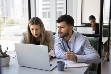 Two colleagues working together, reviewing information, analyzing data, learning new platform engaged in professional task, researching, preparing for presentation using laptop met in modern coworking
