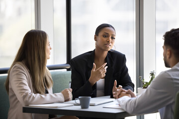 African and European colleagues negotiating, lead formal discussion about business proposal, deal, or project, share point of view, explaining solution, provide information during meeting in office