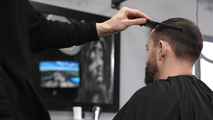 Professional hairdresser styling male client's hair, mirror reflecting classic barber pole, salon...
