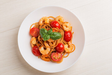 The Italian whole grain spaghetti with shrimp, cherry tomato in a white bowl on wooden table. Top view. Mediterranean cuisine.